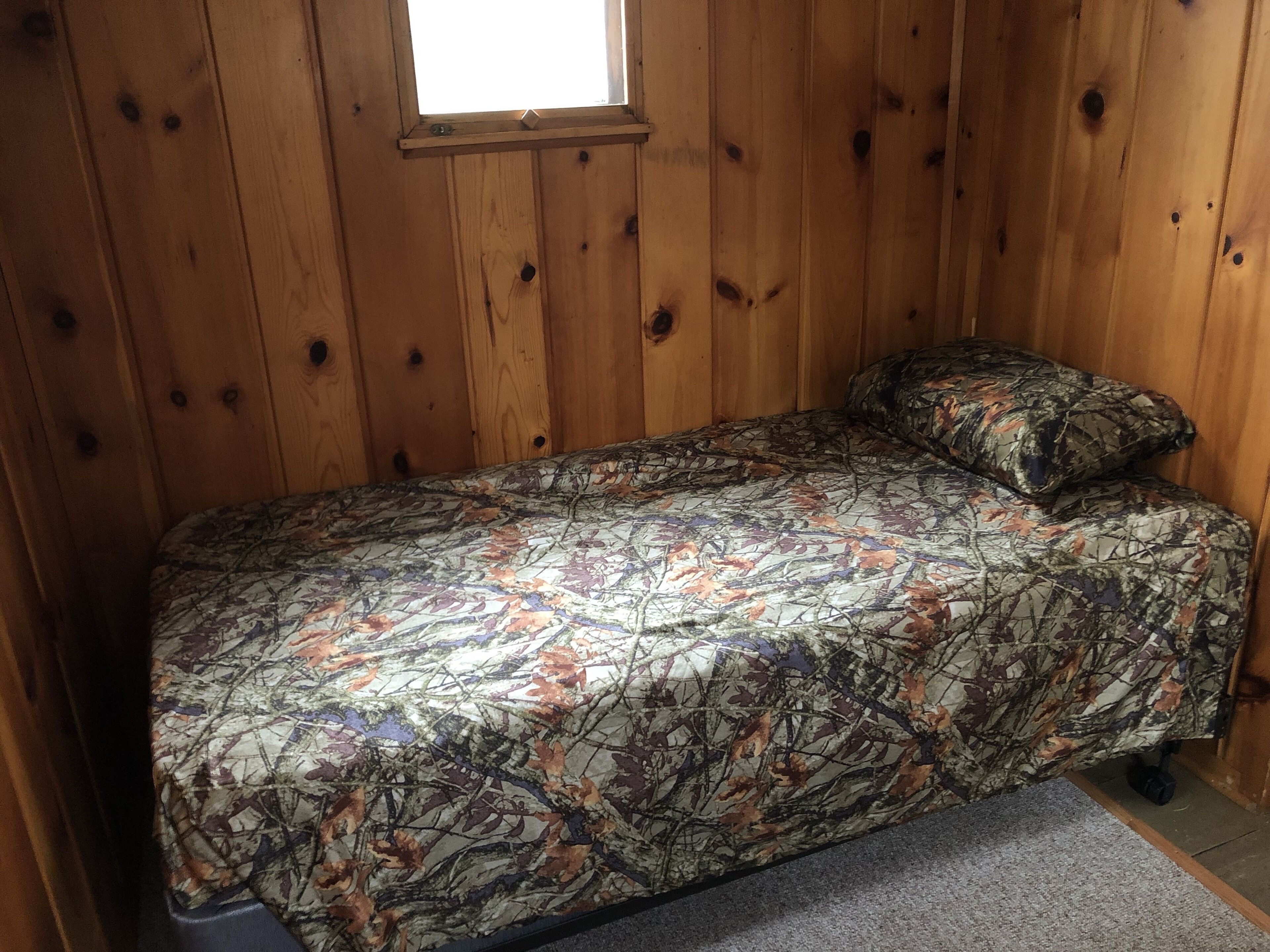 Una habitación pequeña de madera con una cama, una ventana y una puerta.