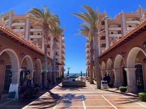 Ein Hotelinnenhof mit Palmen, Sitzgelegenheiten im Freien und Blick auf das Meer.