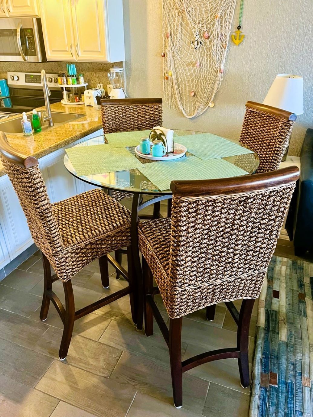 Un coin repas avec une table ronde, quatre chaises en osier, une cuisine en arrière-plan et une décoration murale en macramé.