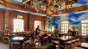 Un restaurant avec de hauts plafonds en bois, des décorations suspendues et une fresque représentant une femme. Les tables et les chaises sont disposées pour accueillir les clients.
