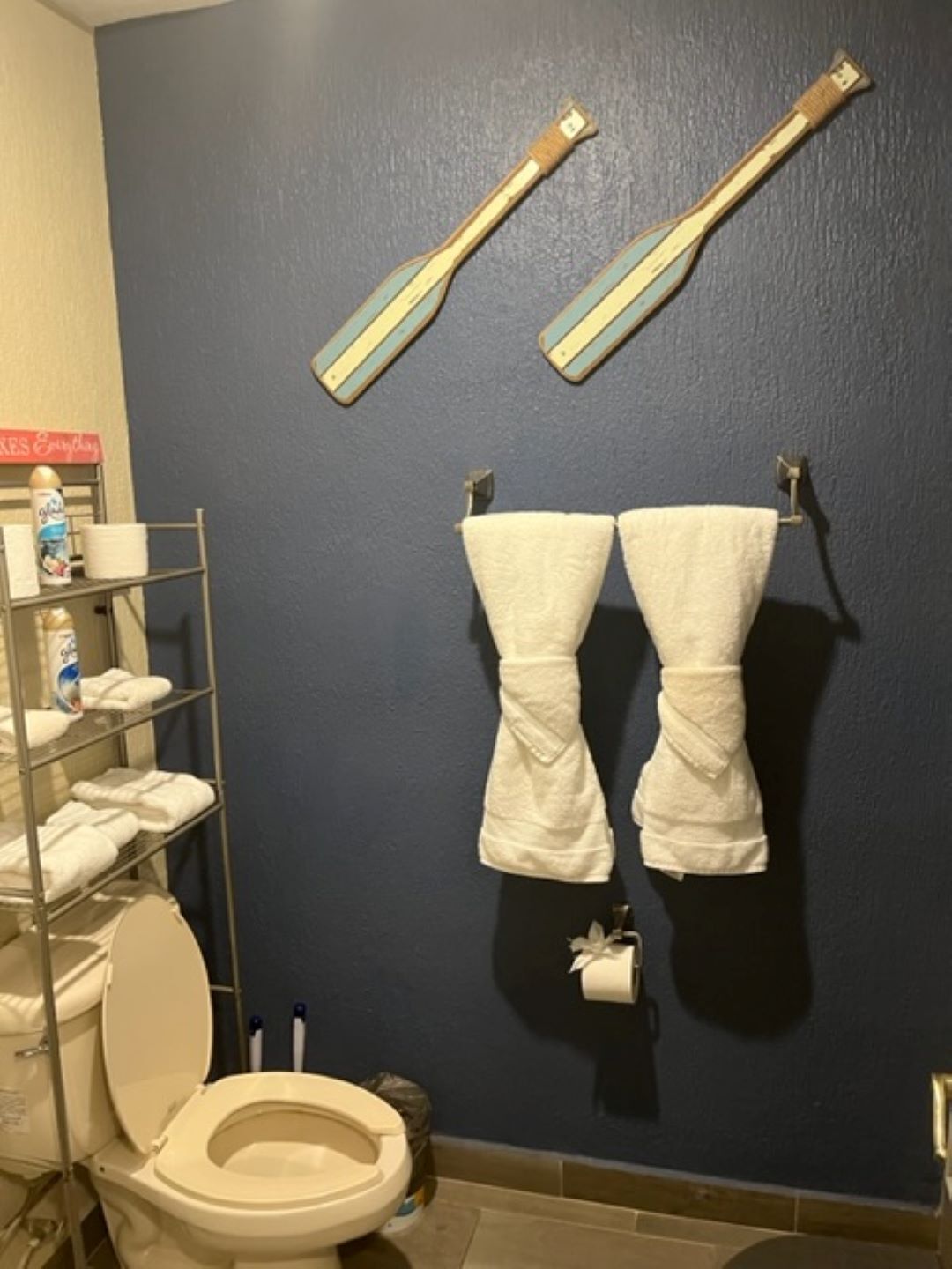 A bathroom with a toilet, a shelf with toiletries, and two towels hanging on hooks.