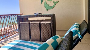 Un balcon agrémenté d’une table en osier, de coussins à rayures et d’un élément décoratif mural.