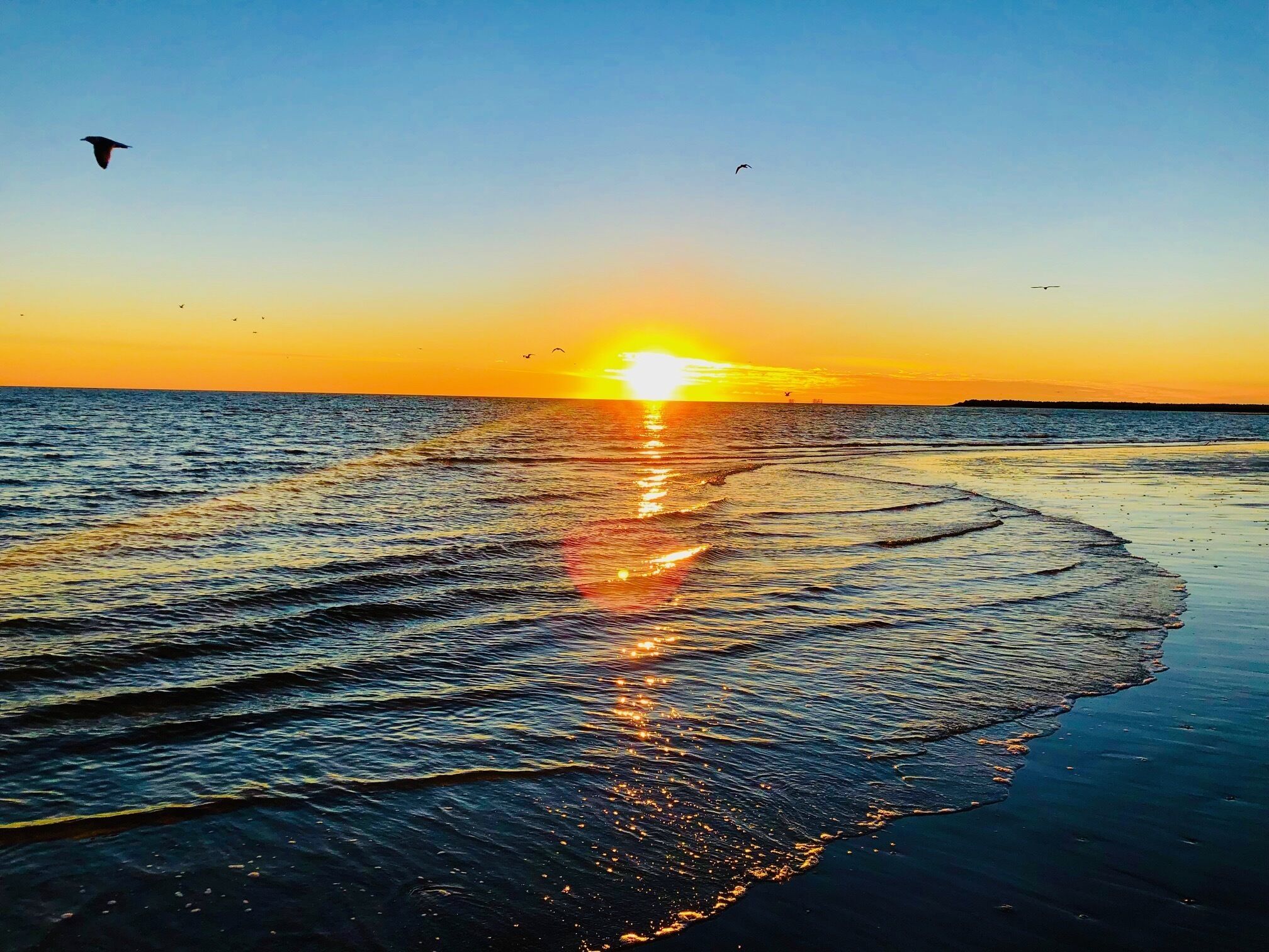 Een strand bij zonsondergang, met golven die de zon weerspiegelen.