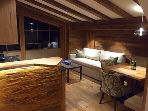 A cozy room with a wooden ceiling, a sofa with cushions, a small table, and a window. - Type 2 -1 bedroom, DG, 2-4 Pax - Pepi's Suites Lechtal Apartments (Holzgau)