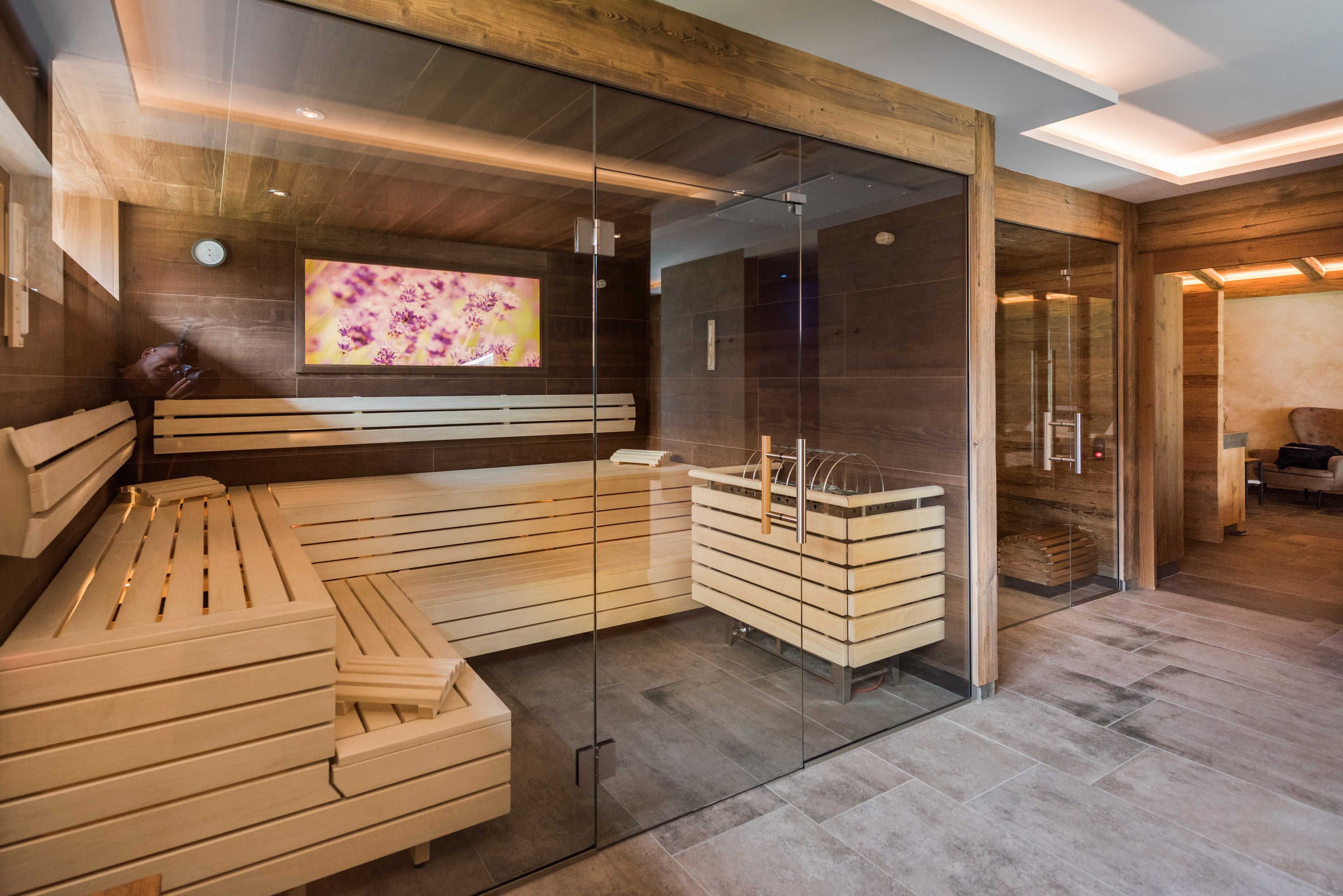 A modern spa room with a wooden bench, glass walls, and a television screen.