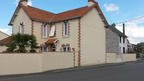 A two-story house with a red-tiled roof, a beige facade with red brick accents, and a small front porch. - Jominiere (Cholet)