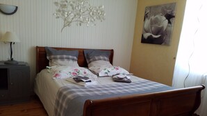 A neatly made bed with floral bedding, a wooden headboard, and a bedside table with a lamp. - Jominiere (Cholet)