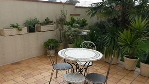 A patio with a round table and four chairs, surrounded by potted plants and a palm tree. - Jominiere (Cholet)