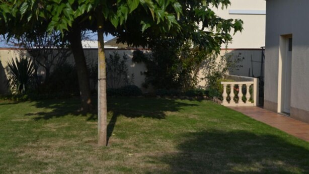 A courtyard with a tree, a white wall, and a building with a balcony. - Jominiere (Cholet)