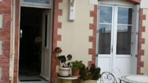 A courtyard with a tiled floor, a white door, a small table with potted plants, and a metal chair. - Jominiere (Cholet)