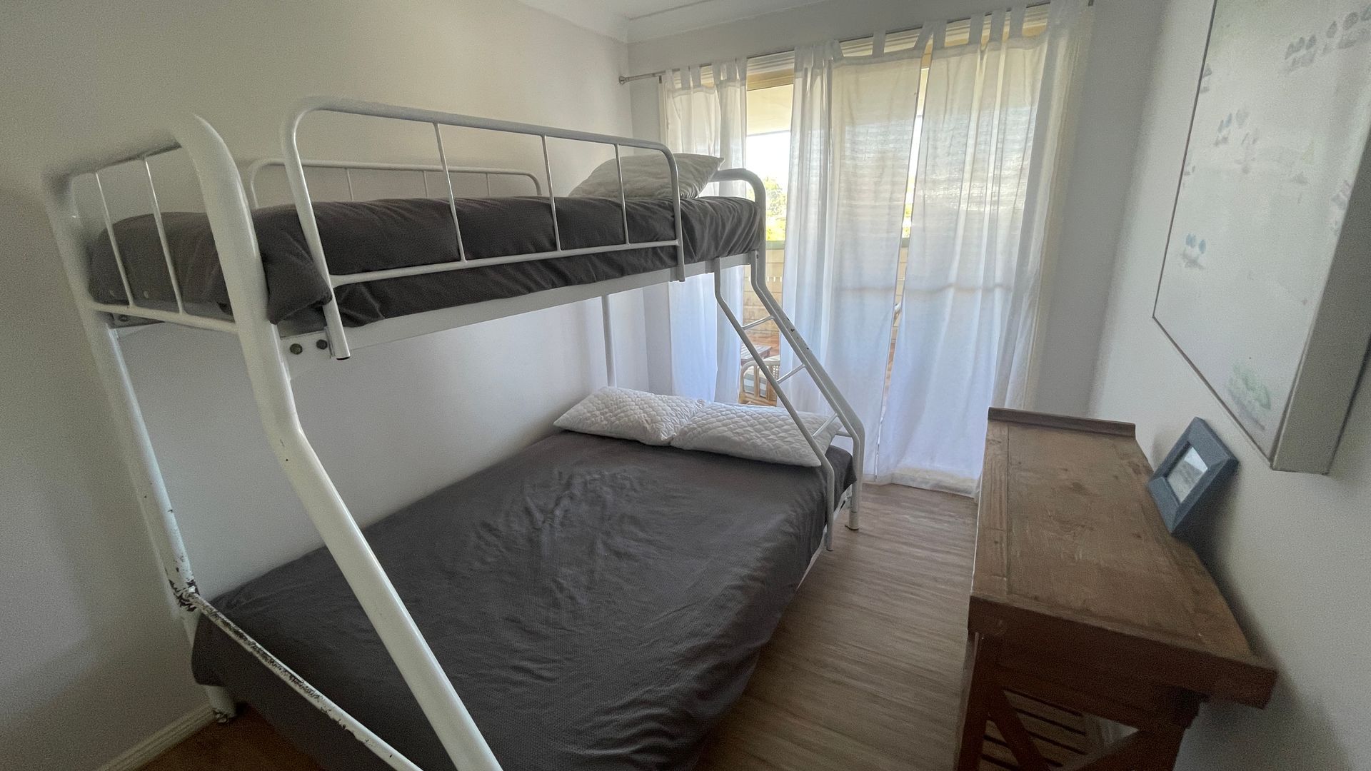 Een stapelbed met een bureau en stoel, een raam met gordijnen en een muur met een foto.