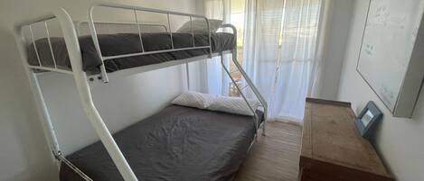 Een stapelbed met een bureau en stoel, een raam met gordijnen en een muur met een foto.