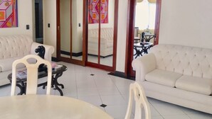 Un salon avec un canapé, une table à manger et des chaises, ainsi qu’une porte-fenêtre coulissante donnant sur une autre pièce.