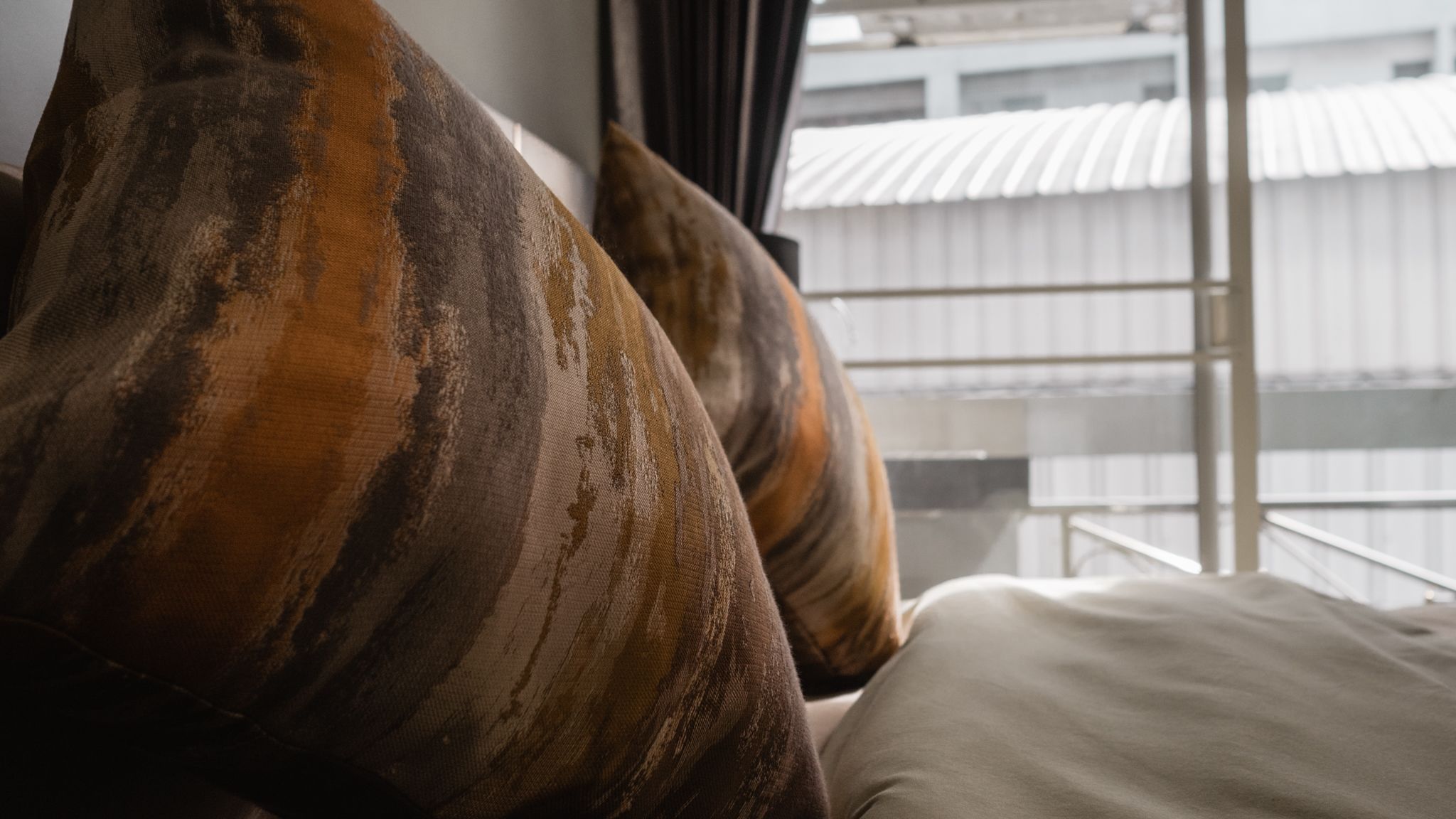 A bed with patterned pillows and a view of a building through a window.
