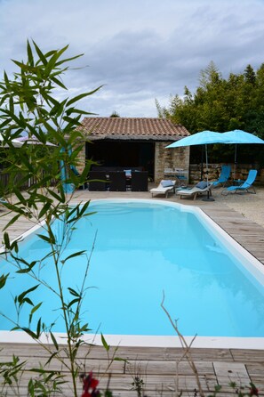 A swimming pool with lounge chairs and umbrellas, surrounded by a wooden deck and stone walls. - Gite Nino near Vallon Pt d'Arc and the village of Barjac. (Barjac)
