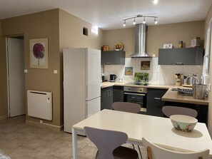 A modern kitchen with a white refrigerator, oven, and stove, a dining table with chairs, and a window with blinds. - Gite Nino near Vallon Pt d'Arc and the village of Barjac. (Barjac)