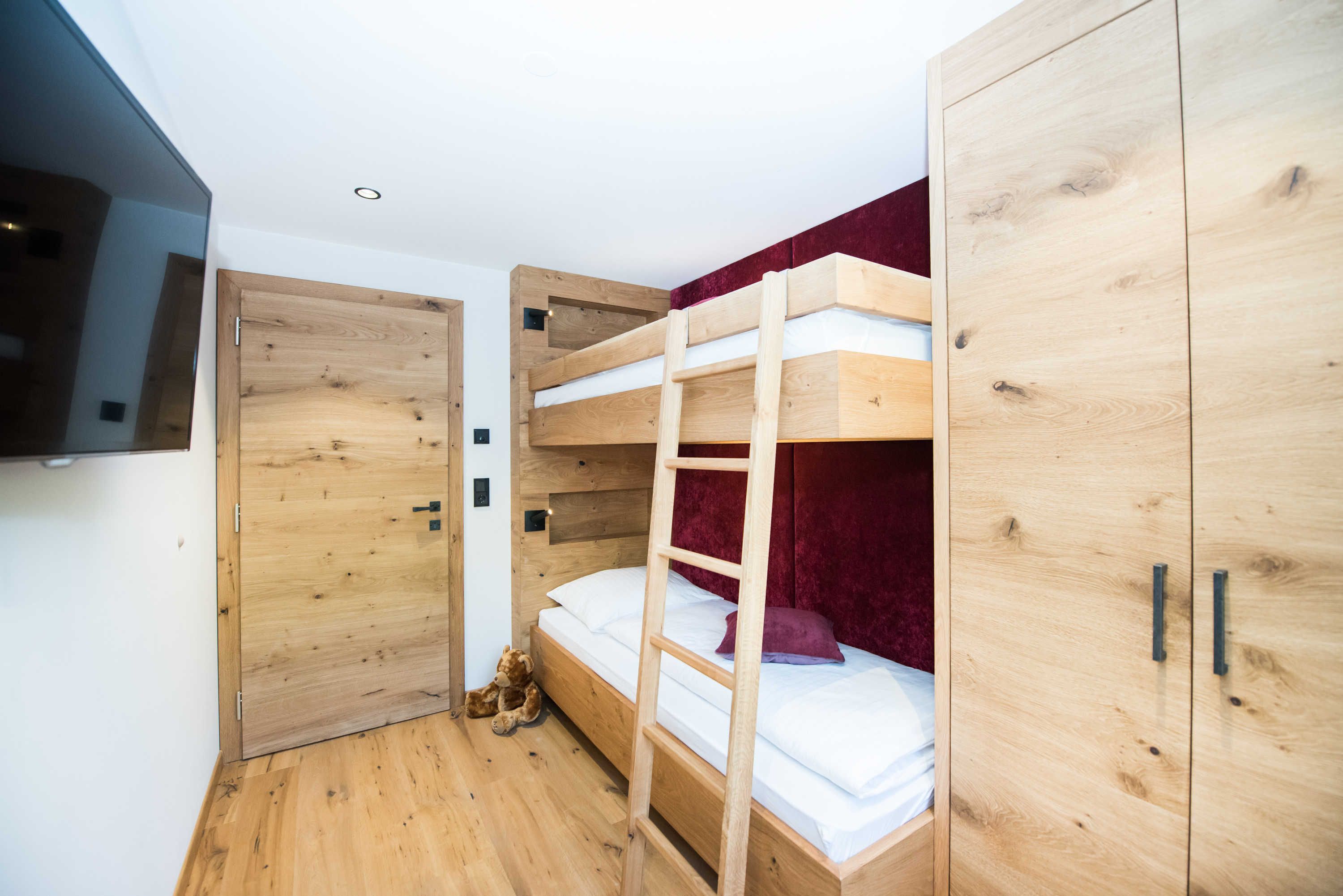 A bunk bed with a ladder, a wooden wardrobe, and a teddy bear on the floor.