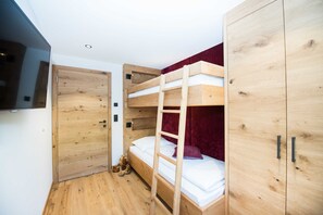 A bunk bed with a ladder, a wooden wardrobe, and a teddy bear on the floor.