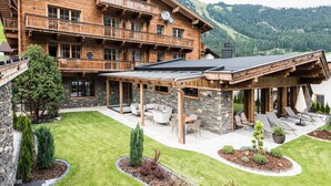 Una cabaña de madera con un patio, mobiliario exterior y vistas a las montañas.
