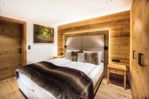 Une chambre à coucher avec une tête de lit en bois, un lit recouvert de draps blancs, un plaid en fourrure et une table de chevet avec une lampe.