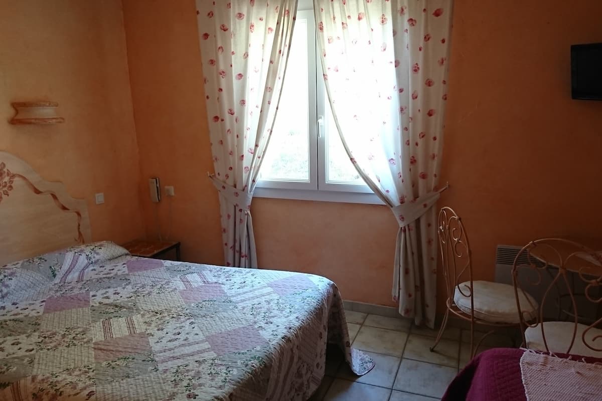 Un dormitorio con cama, una silla, un televisor y una ventana con cortinas.