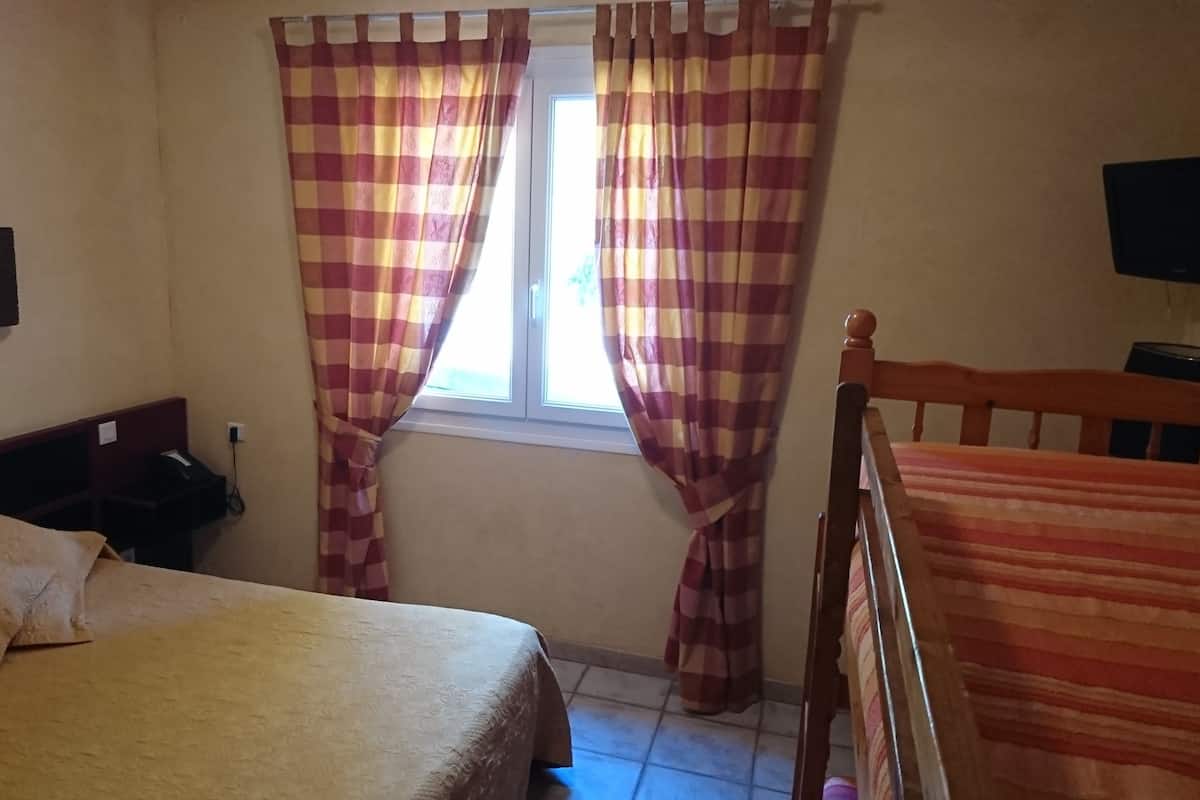 Una habitación con cama, una silla, ventana con cortinas a cuadros y televisión en la pared.