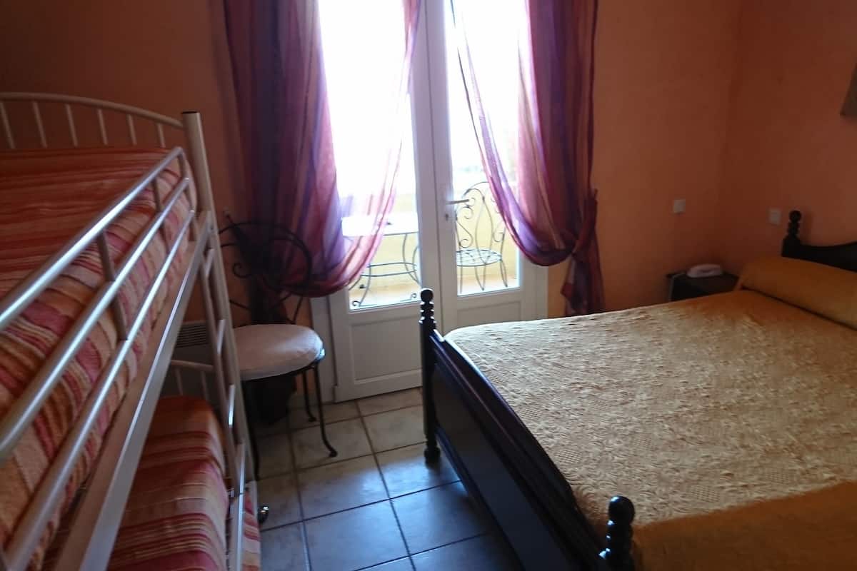 Un dormitorio con cama, una silla, una mesita y una ventana con cortinas.