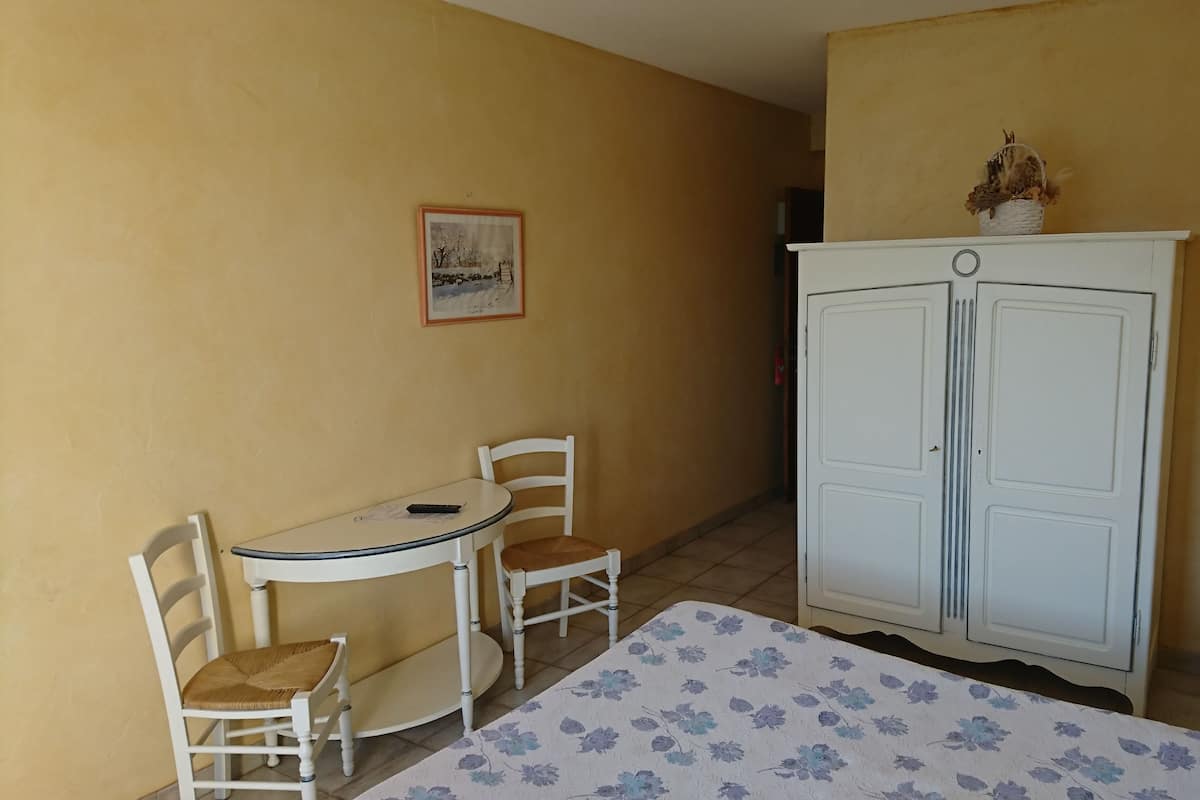 Una habitación con cama, una mesita con sillas, un armario y un cuadro en la pared.