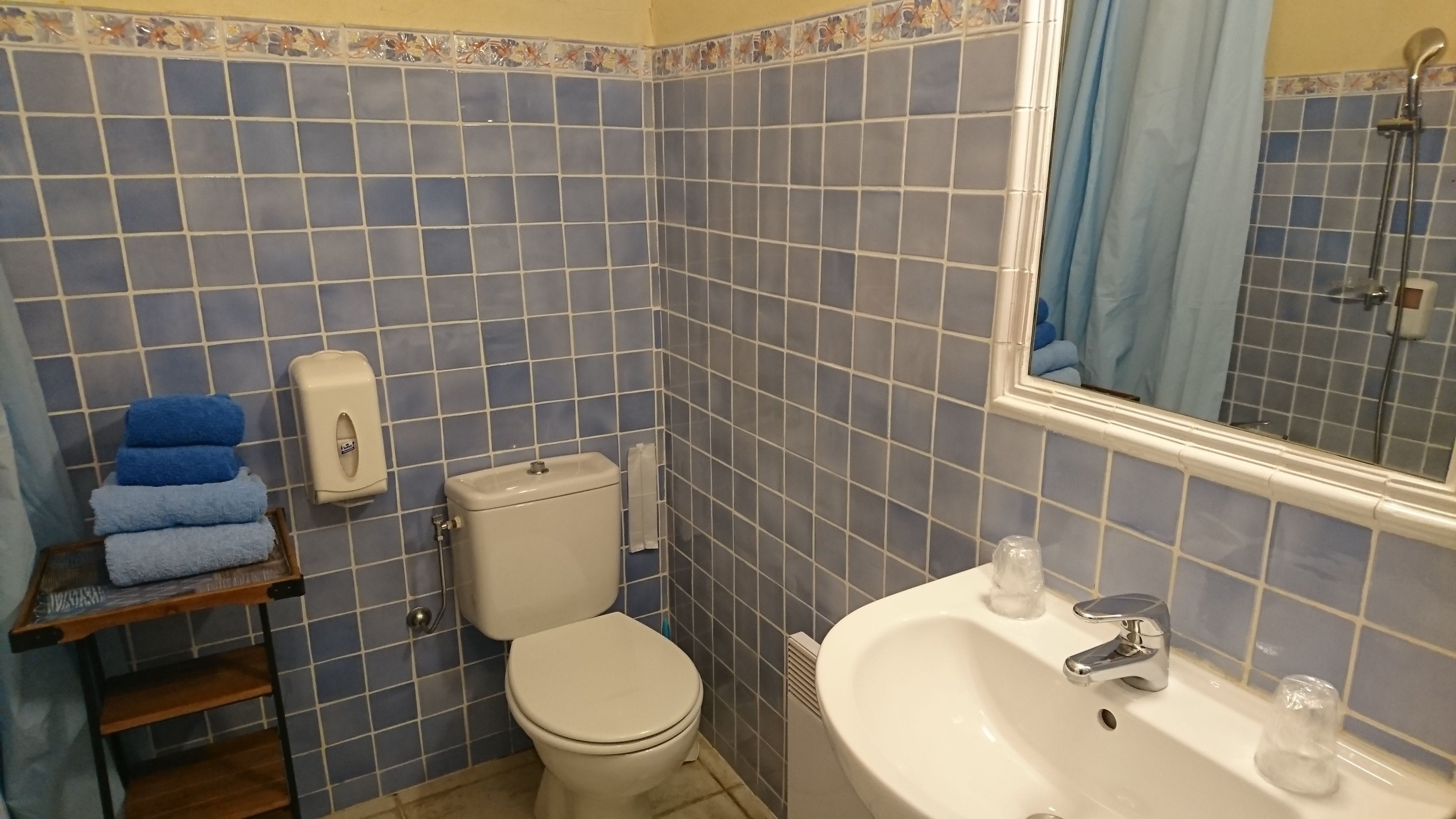 Un baño con paredes de azulejos azules, un inodoro, un lavabo y un estante con toallas.