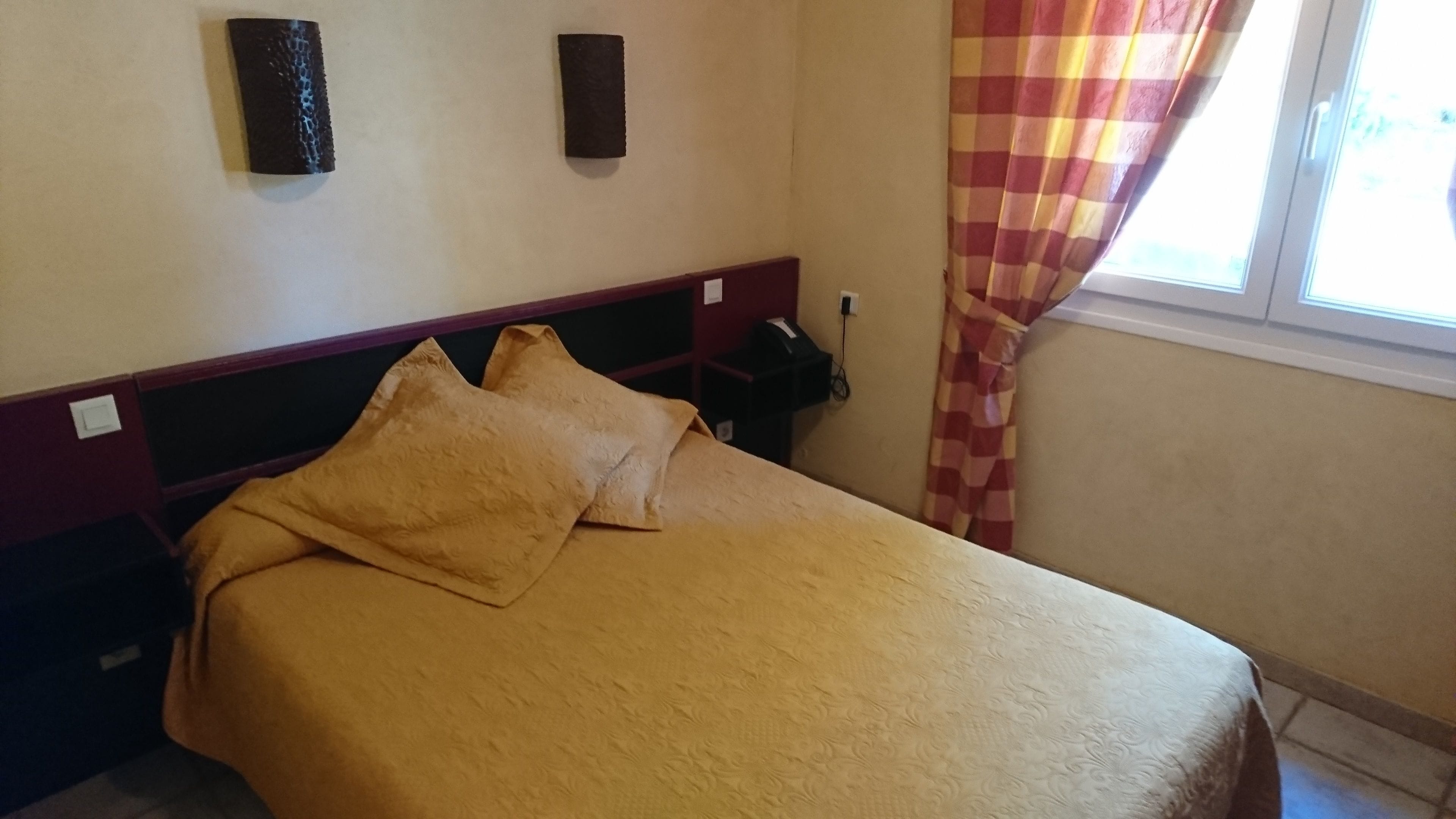 Un lit avec une tête de lit, une table de chevet et un téléphone fixé au mur.