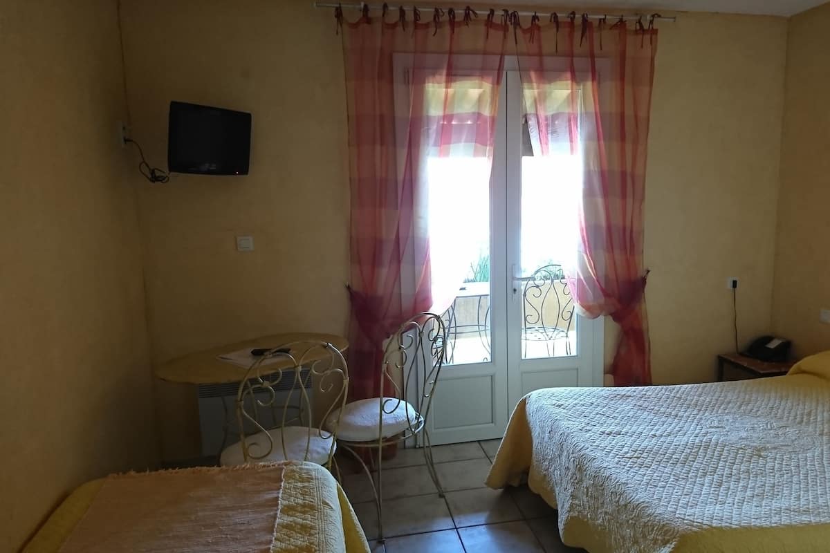 Habitación con dos camas, una mesita, una silla, televisión montada en la pared y ventana con cortinas.