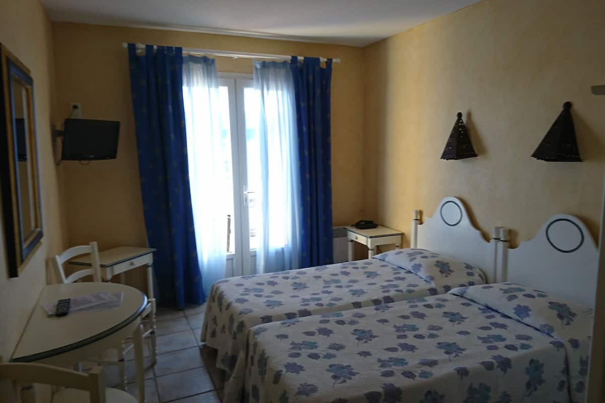 Habitación de hotel con dos camas, un escritorio, una silla y una ventana con cortinas.