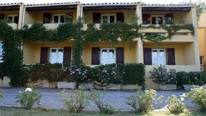 Un edificio de dos pisos con fachada amarilla, varios balcones y un jardín con flores y arbustos.