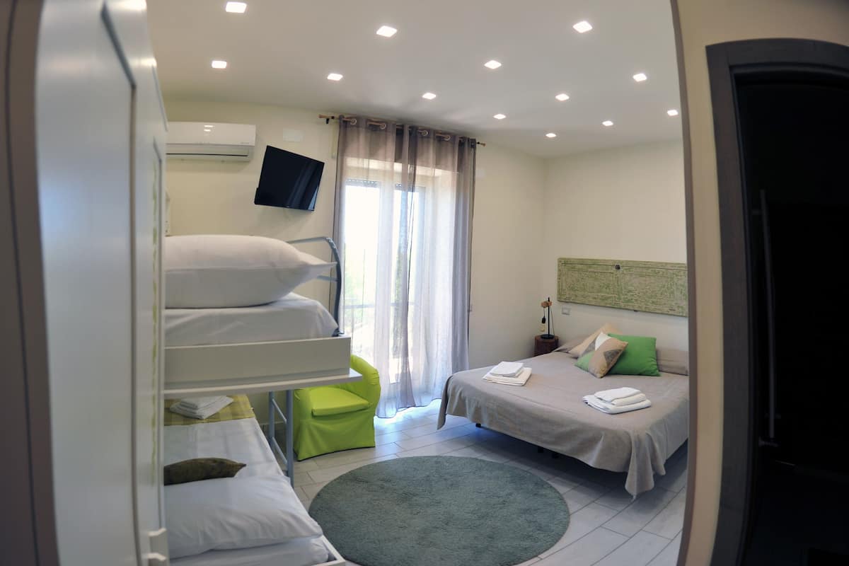 Hotelkamer met stapelbedden, een eenpersoonsbed, een groene stoel, een rond vloerkleed en een wandtelevisie.