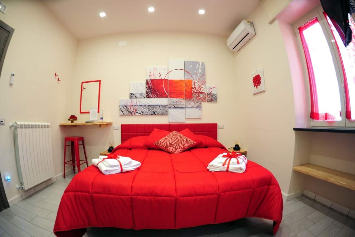 Een moderne slaapkamer met een rode sprei, een grote spiegel en abstracte wanddecoratie.