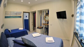 A hotel room with two beds, a desk, a TV, and a bathroom door. - B&B Guest Armonie (Torre del Greco)