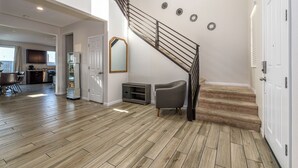 Amplia sala de estar con suelo de madera, una escalera, un sillón gris y una cocina al fondo.