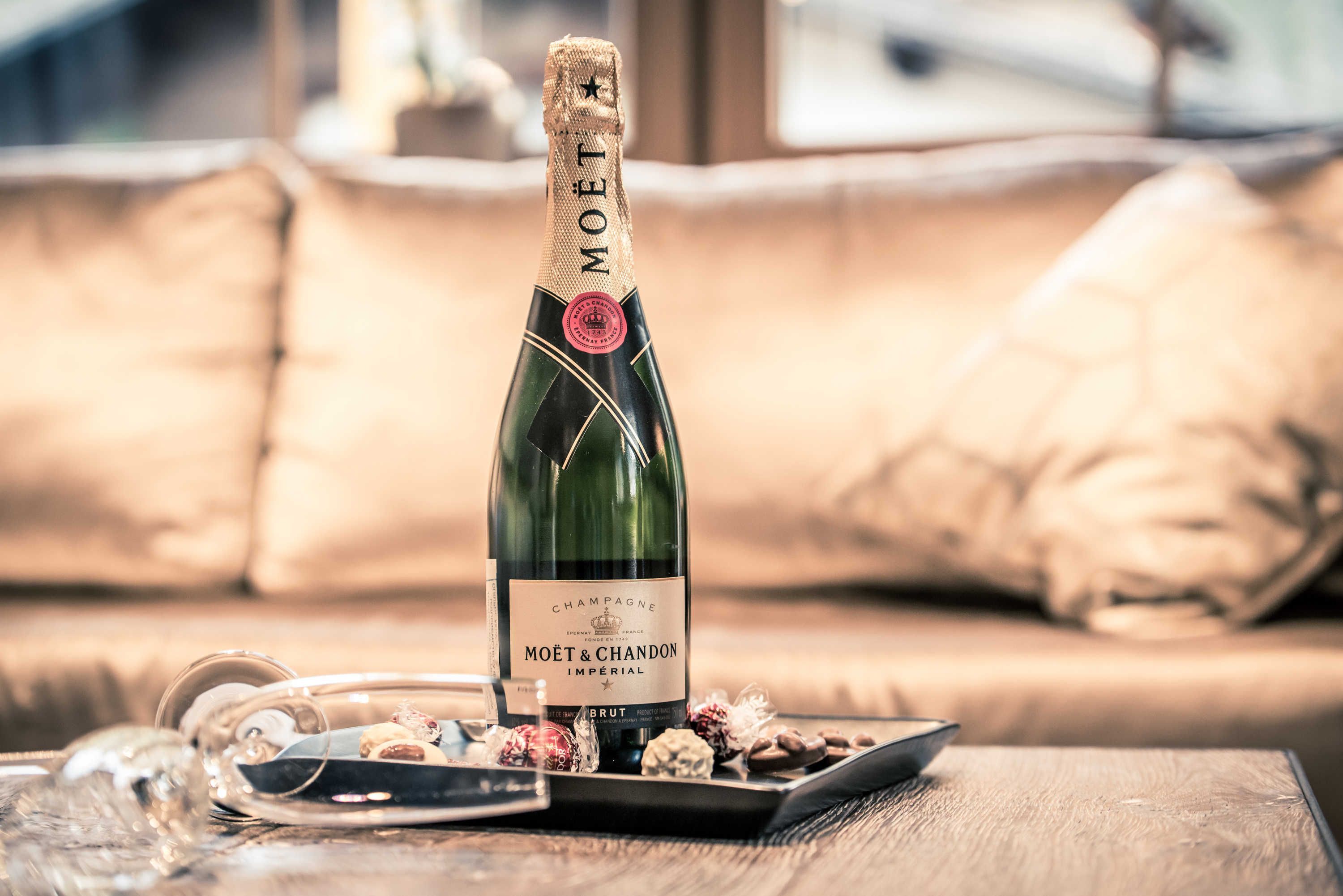 A bottle of Moët & Chandon Imperial Brut champagne on a wooden table with chocolates and a glass.