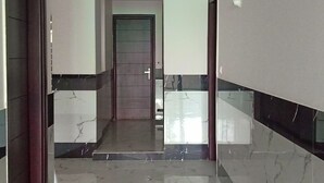 A hallway with a marble floor and walls, leading to a door with a glass panel.