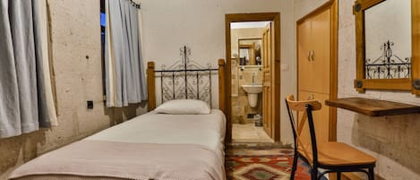 A bedroom with a bed, a chair, a wooden wardrobe, a mirror, and a bathroom visible through an open door.