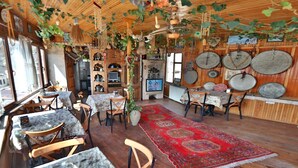 A rustic interior with wooden walls, a dining area with a red patterned rug, and various decorative items including plates and hanging ornaments. - Kookaburra Hotel (Nevsehir)