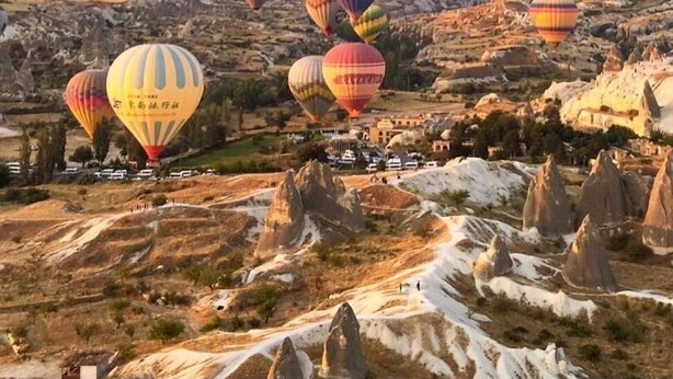 A landscape with numerous hot air balloons over a rocky terrain with unique rock formations. - Kookaburra Hotel (Nevsehir)