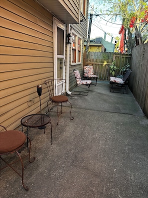 Un jardin avec un espace patio comprenant des chaises et une table en métal, une clôture en bois et une maison recouverte de bardage.