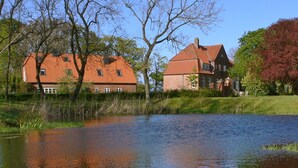 A house with a red roof and brick walls, situated next to a calm body of water with reflections. - Vacation on the manor - small cozy apartment near the Baltic Sea (Waabs)
