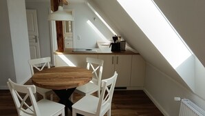 A dining area with a round wooden table and white chairs, a kitchen with a skylight, and a white radiator. - Vacation on the manor - small cozy apartment near the Baltic Sea (Waabs)