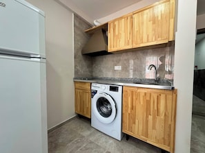 A compact kitchen with a washing machine, wooden cabinets, and a built-in oven. - Akca Apart Otel (Antalya)