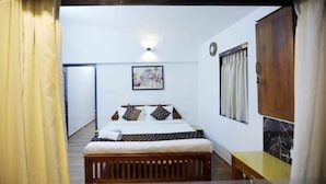 A bedroom with a bed, a bedside table, a wall-mounted light, and a door. - Cherry Blossom Homestay (Kodaikanal)