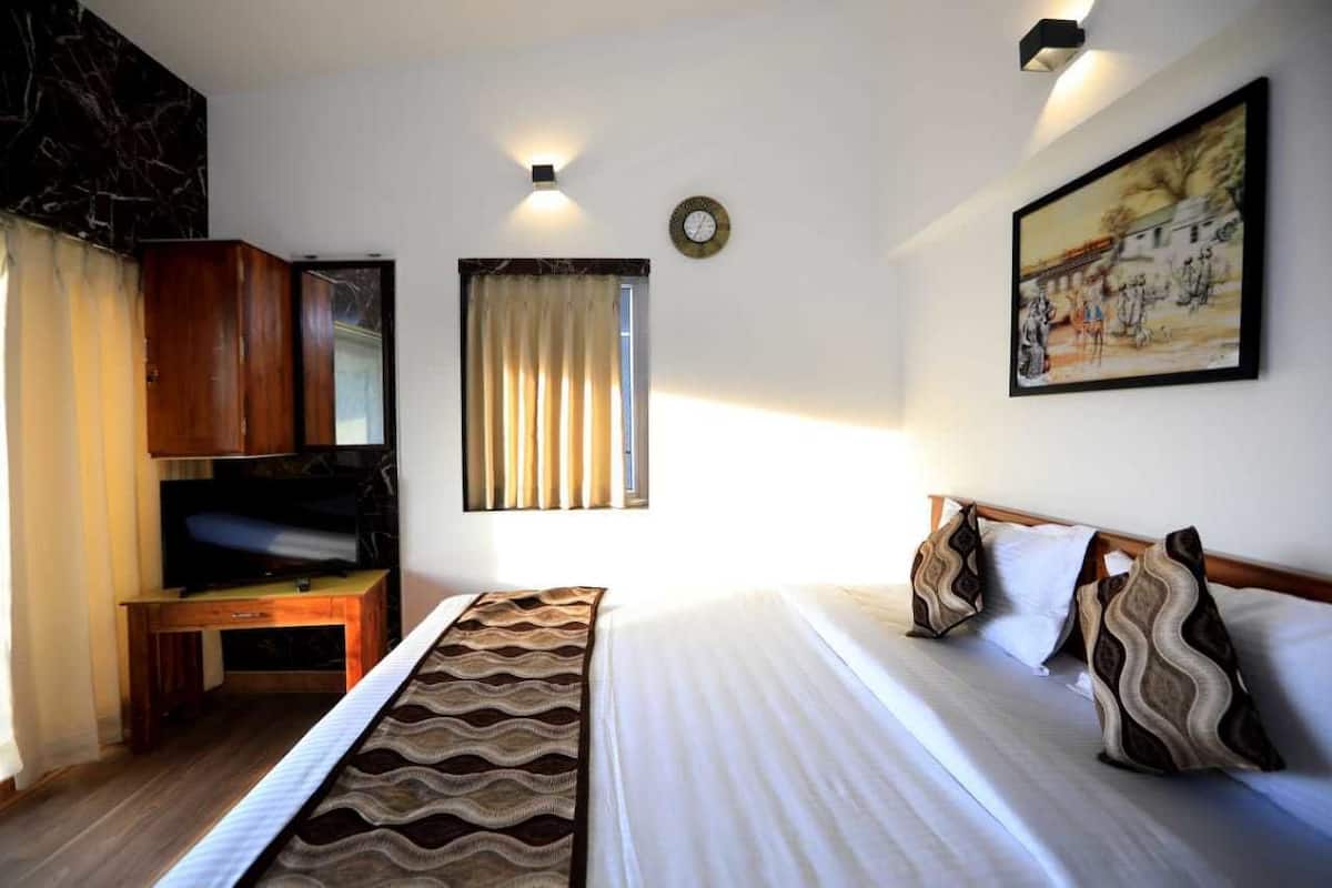 A hotel room with a bed, a desk with a television, a window with curtains, a wall clock, and a painting.