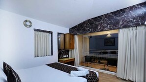 A hotel room with a bed, a desk, a chair, a balcony with a view, and a marble wall. - Cherry Blossom Homestay (Kodaikanal)