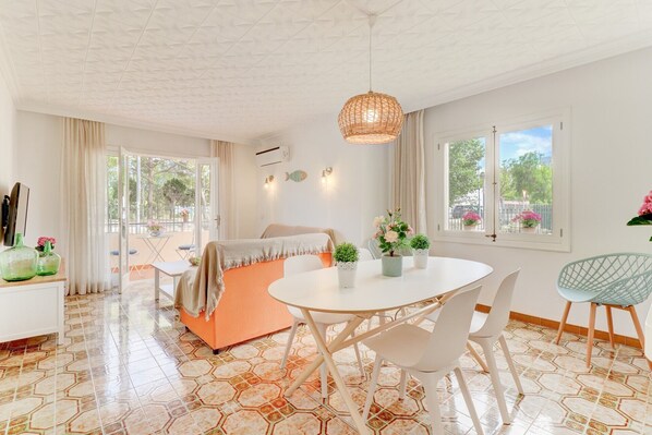 A bright, well-lit room with a round dining table, white chairs, a sofa, and a hanging light fixture.